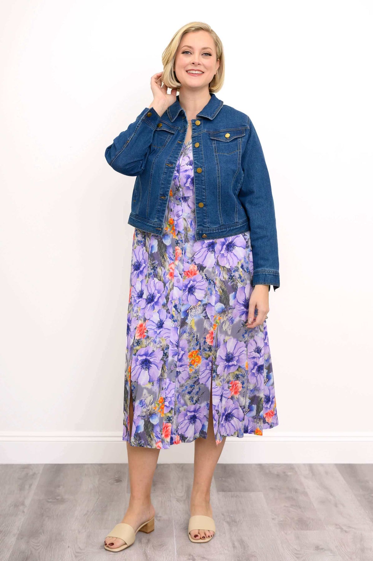Woman posing with her hand in her hair while wearing a purple floral dress and denim jacket