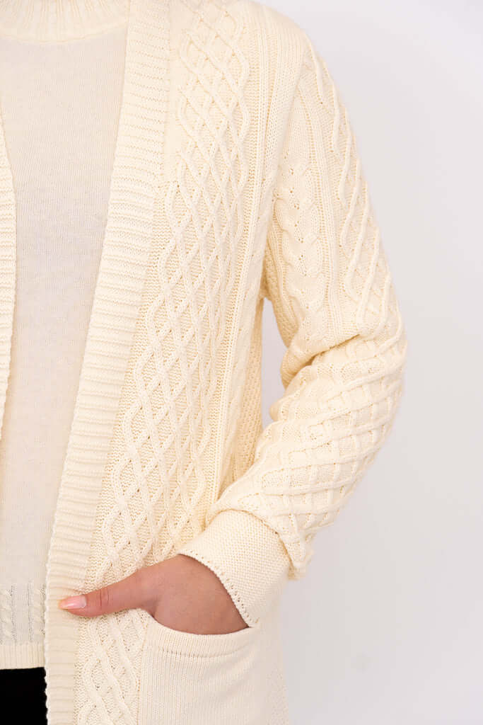Close-up of cream cable knit cardigan showing textured pattern and front pocket detail