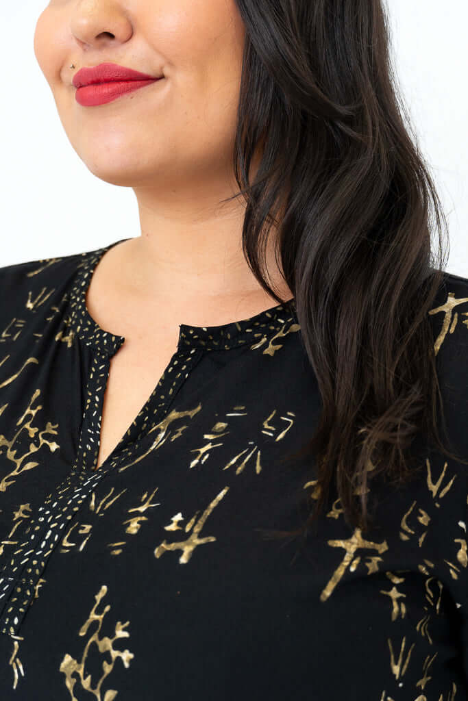 Detail view of gold batik pattern and V-neck on black blouse