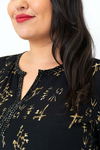 Detail view of gold batik pattern and V-neck on black blouse