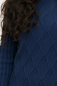 Side profile shot of a woman wearing a dark indigo long sleeve cable knit sweater tunic with boots.