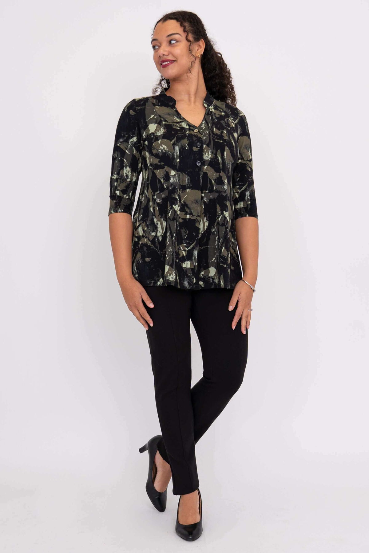 Woman looking sideways wearing the black and green abstract patterned top, black pants, and heels