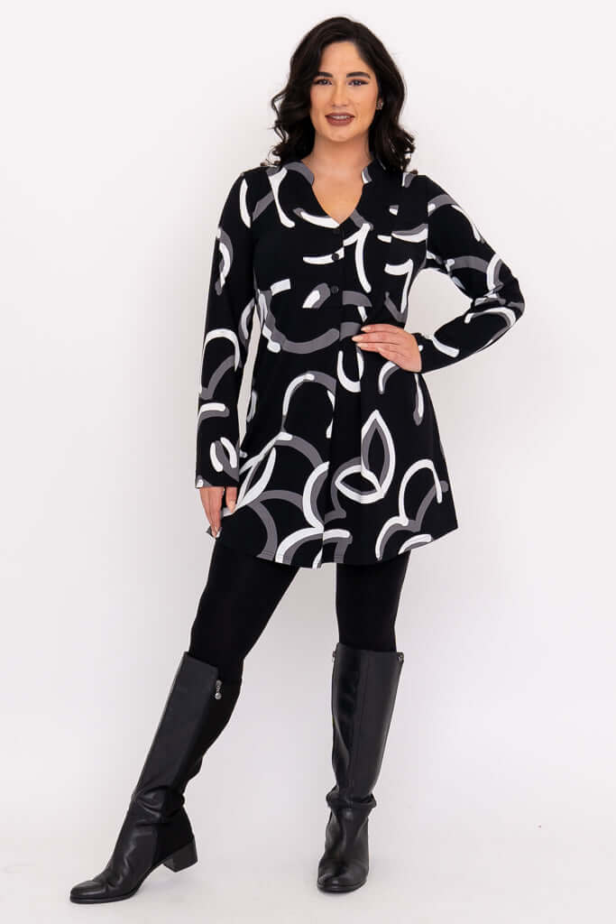 Woman standing with hand on hip in black tunic, white and grey pattern, boots.