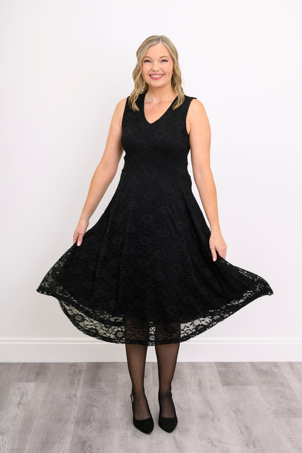 Woman playfully swaying her sleeveless black lace dress and smiling