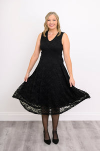 Woman playfully swaying her sleeveless black lace dress and smiling