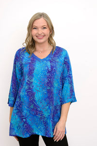 Front view of woman wearing a blue v-neck patterned blouse and black pants against a white background