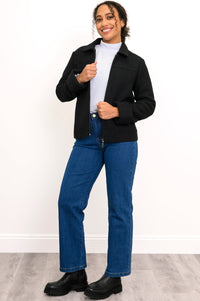 Woman wearing a black jacket, white shirt, blue jeans, and black shoes on a white background, front view