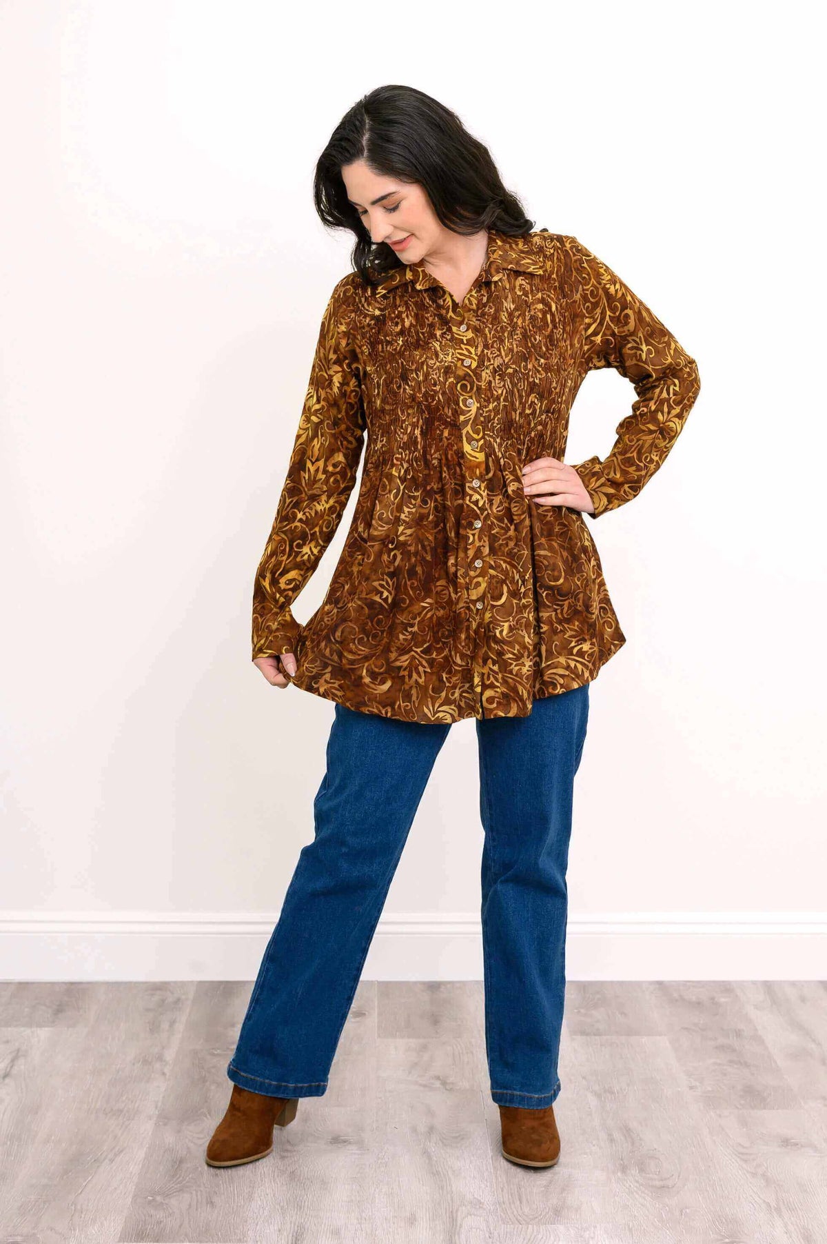 Woman displaying flared pleats of autumn gold smocked shirt paired with jeans and boots