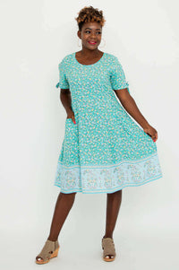 Woman displaying the flowy skirt of a teal floral dress with border print