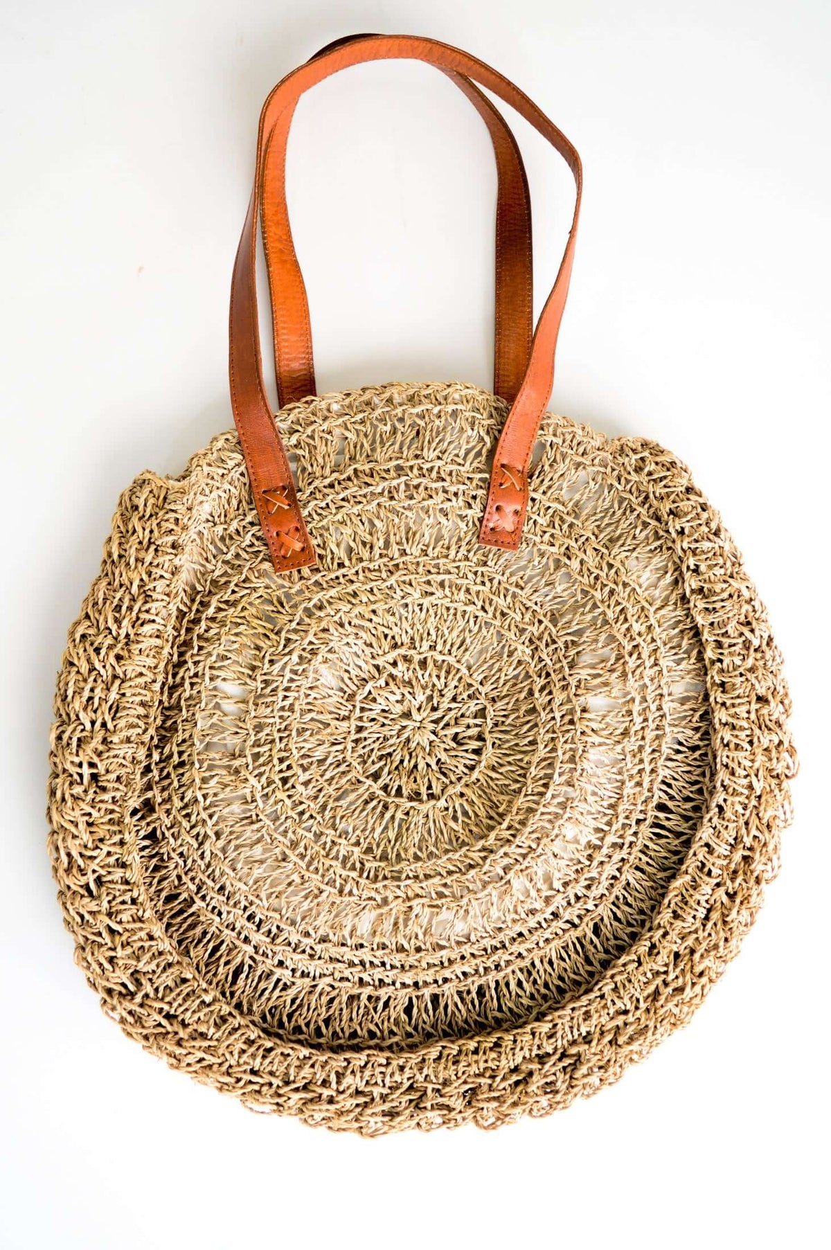 Circular rattan tote bag with long brown leather straps displayed flat