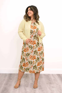 Woman in floral dress and yellow cardigan smiling and looking to side