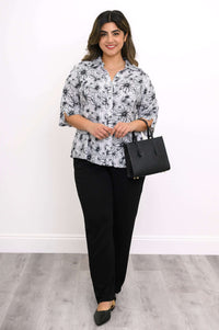 Woman standing in floral blouse and black pants holding a black handbag