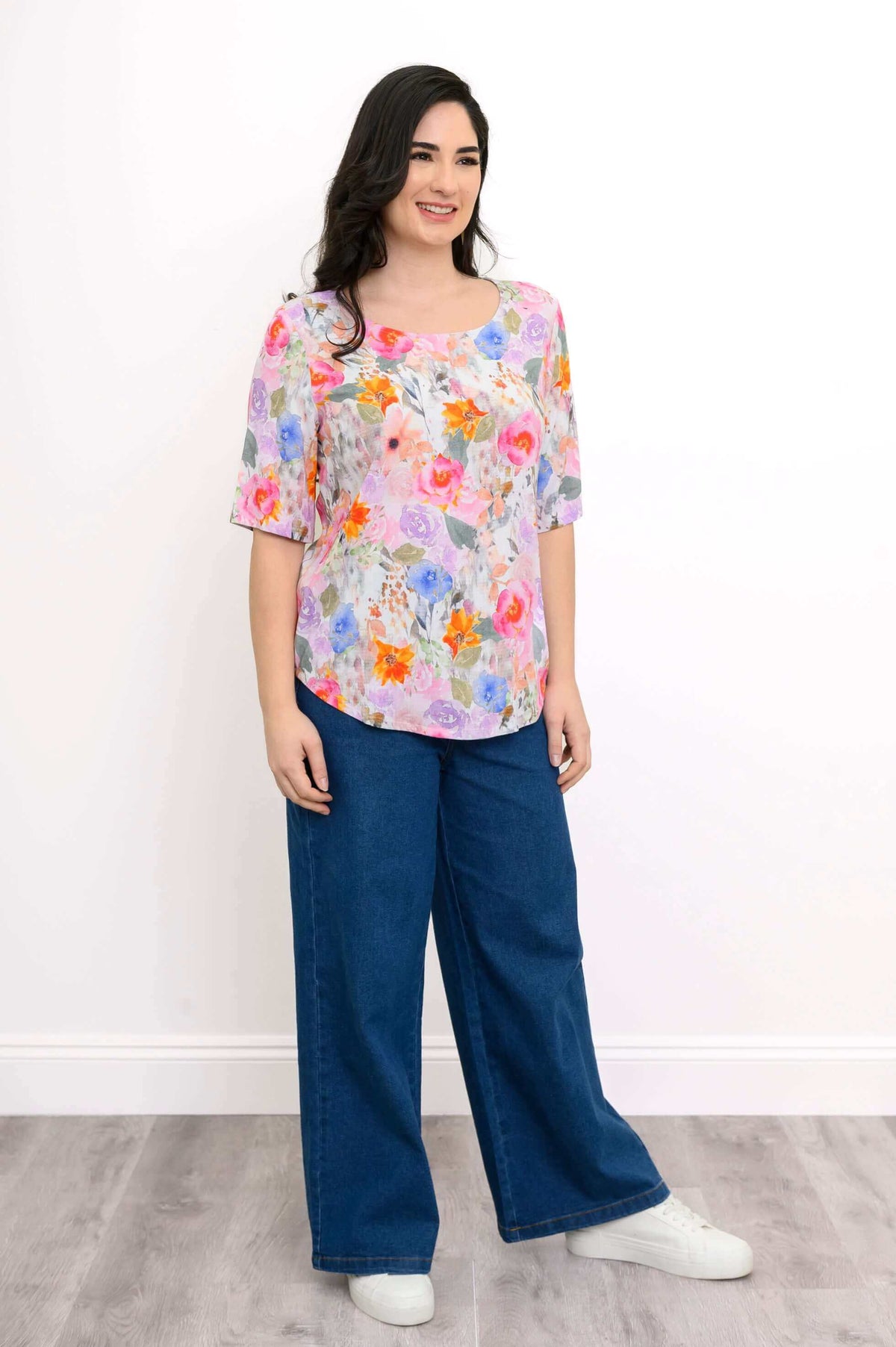 Woman in floral blouse and jeans smiling, angled front view