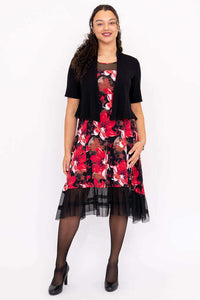Woman in floral mesh-hem dress with short black cardigan, standing and smiling