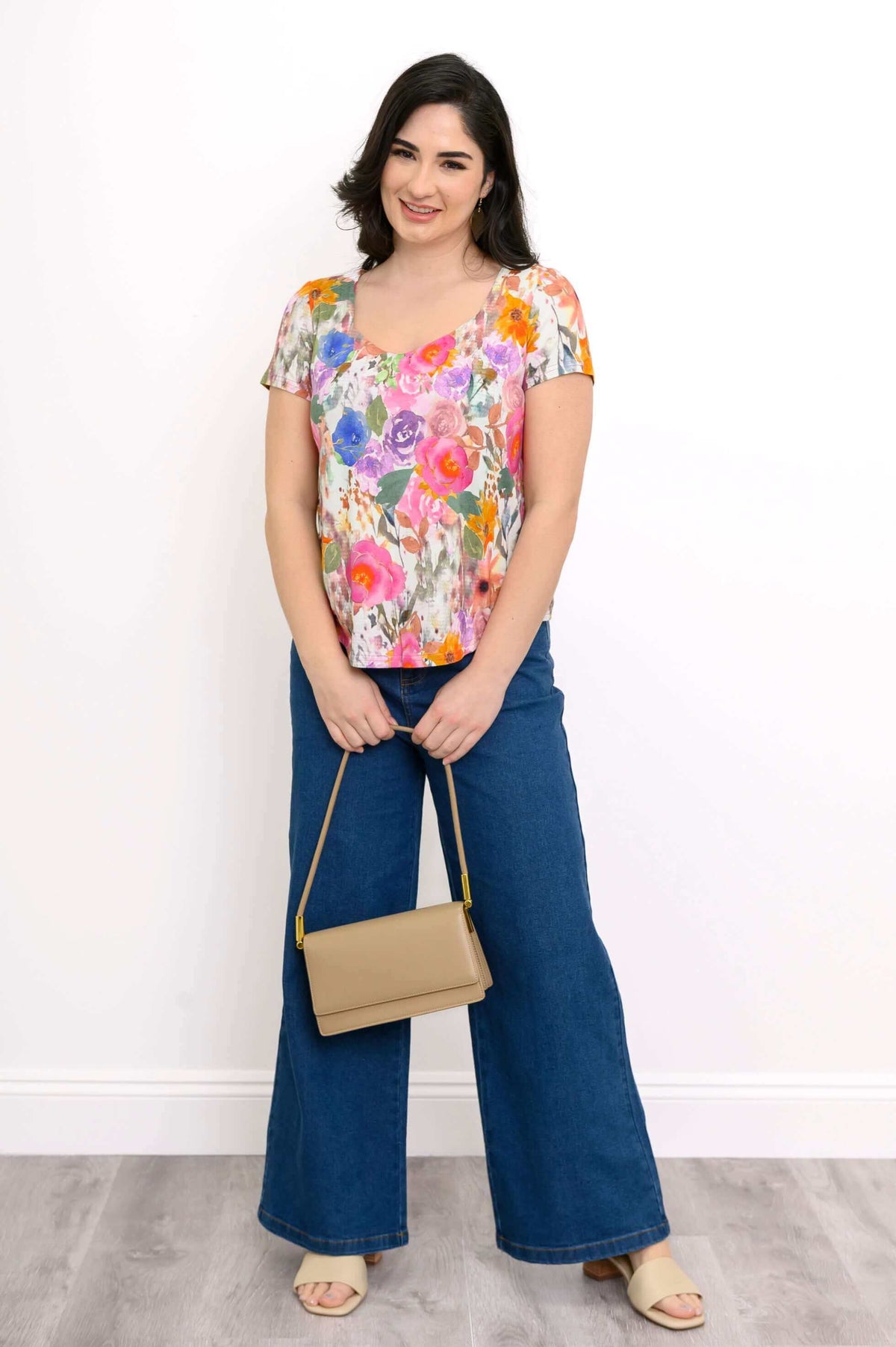 Woman in floral top and jeans holding a tan purse