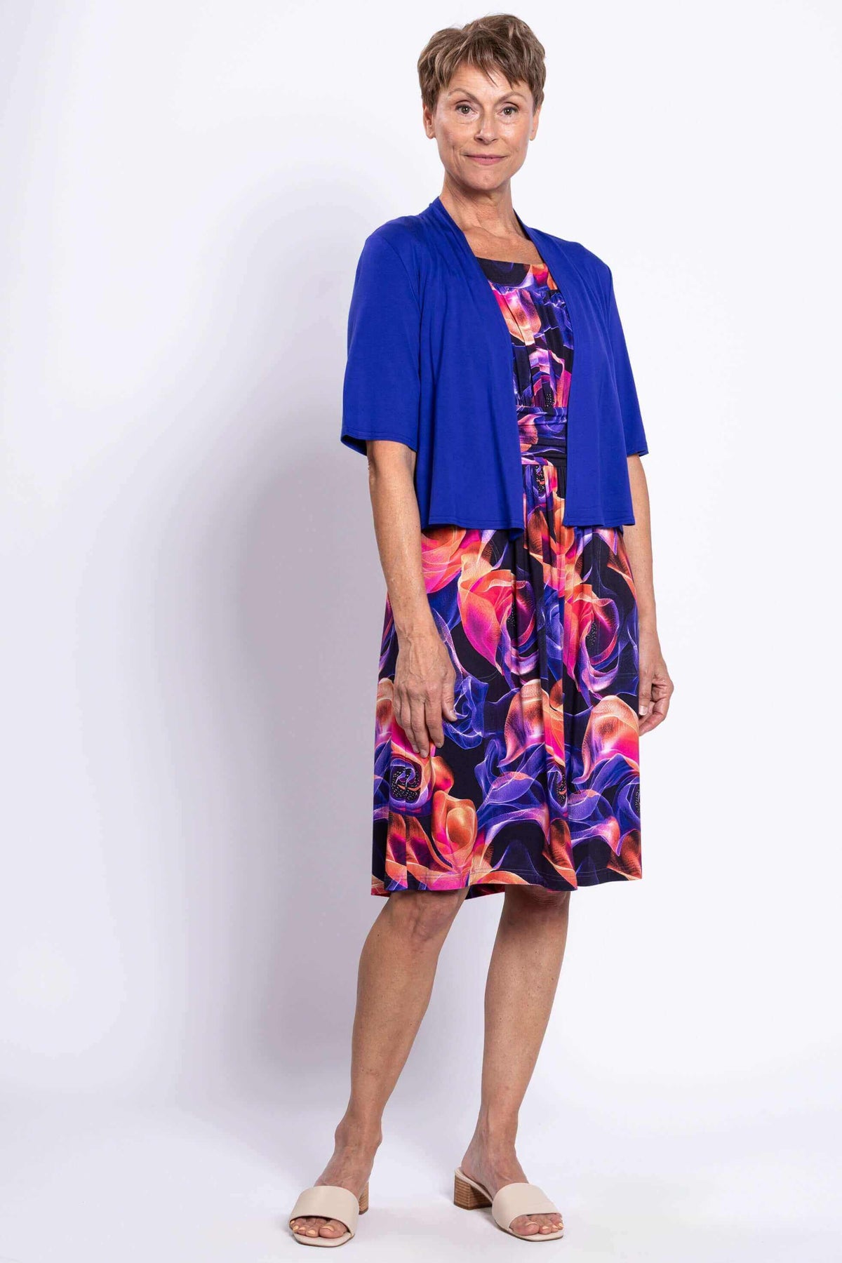 Woman wearing a vivid floral swirl dress paired with a royal blue short cardigan