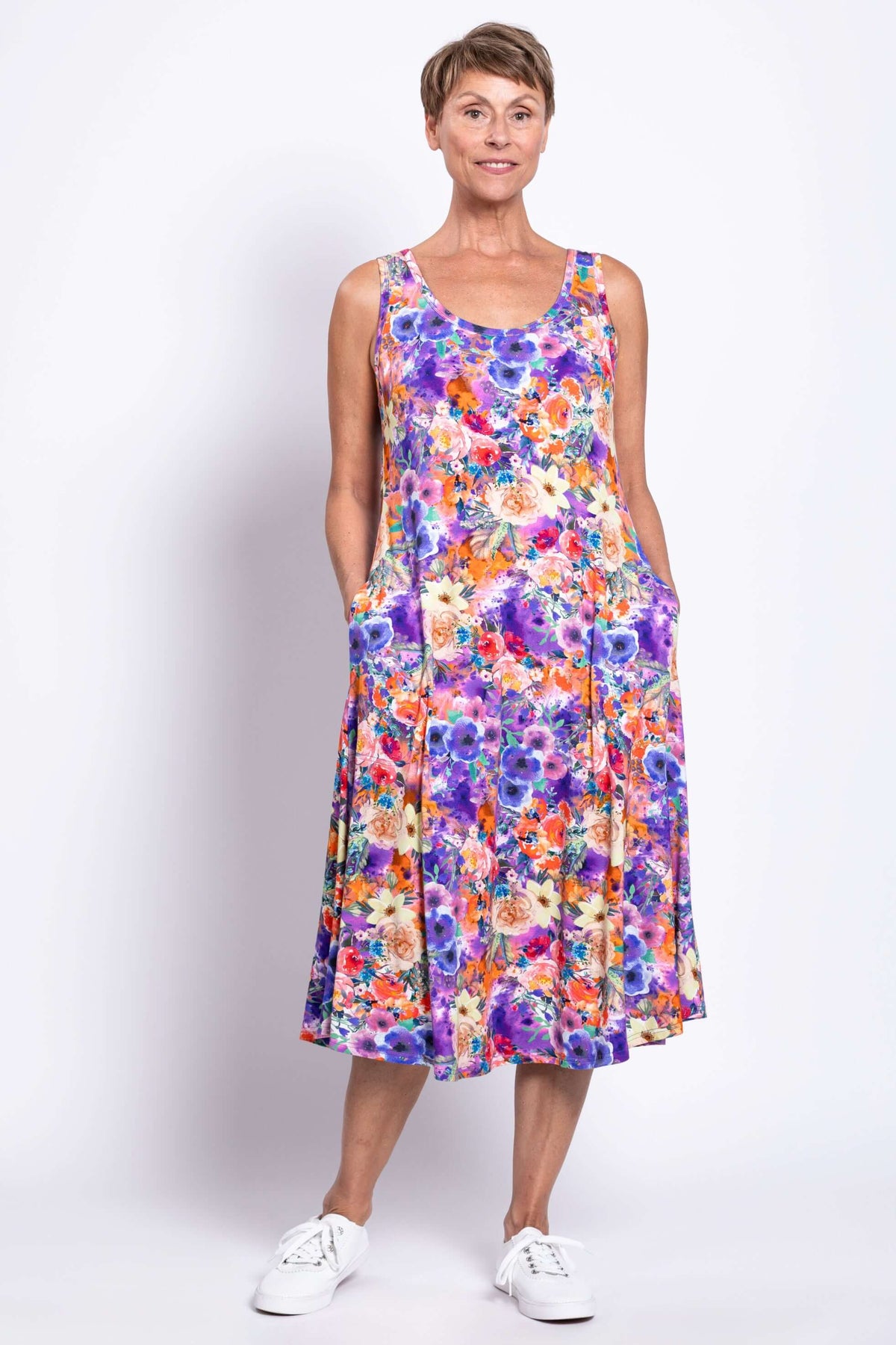 Woman posing in vibrant floral tank dress with hands in side pockets