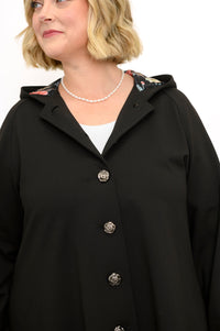 Front view of woman wearing black coat with buttons and pearl necklace against a white background
