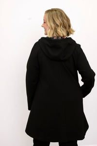 Back view of woman wearing black coat with hood, floral lining and black pants against a white background