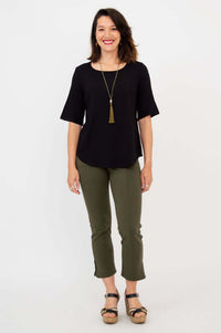 Woman wearing black blouse standing front-facing with olive pants