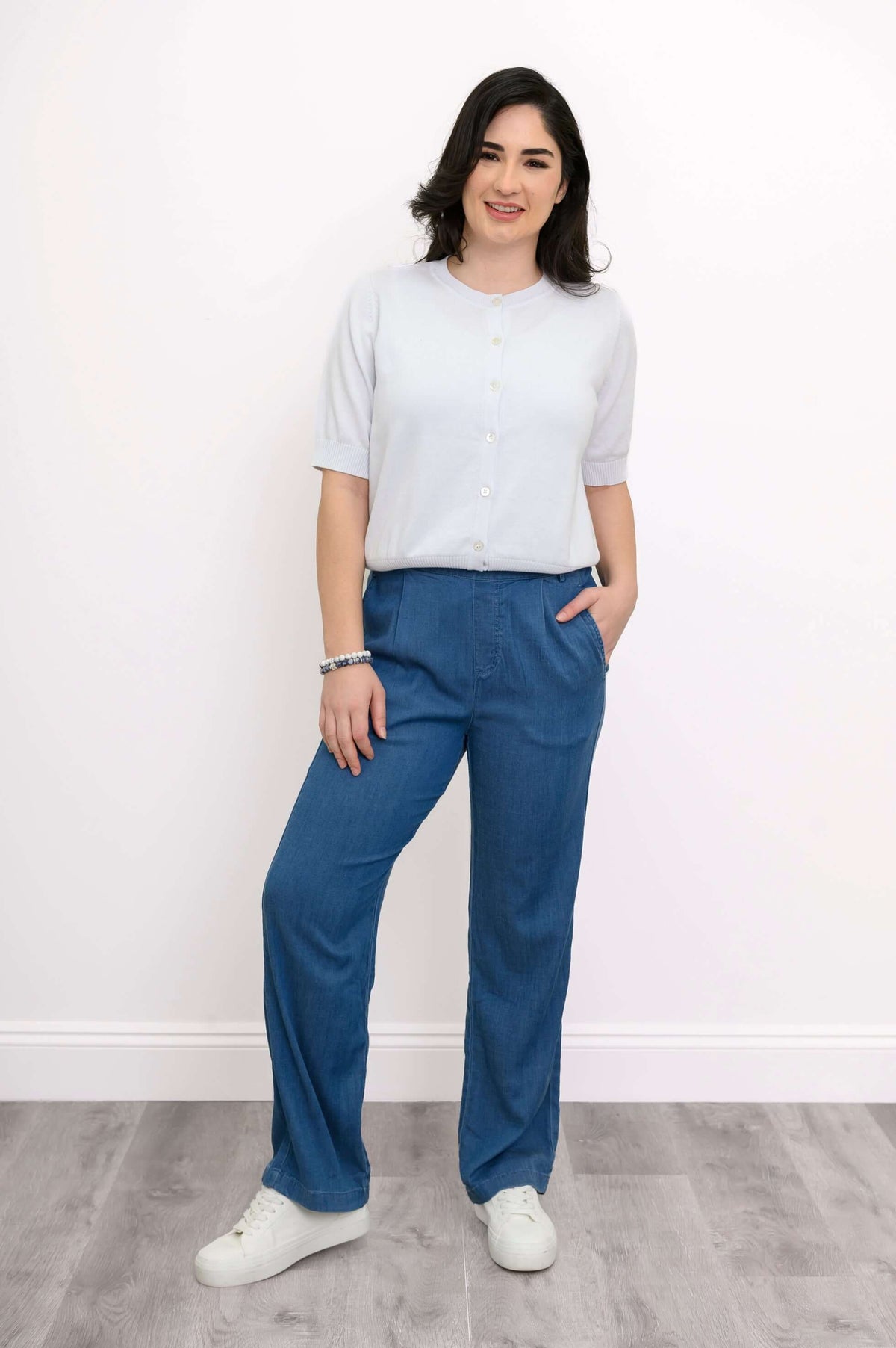 Woman in a buttoned short-sleeve cardigan and blue pants, standing front-facing