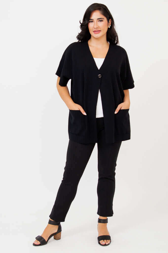 Woman in black cotton cardigan, relaxed fit with hands in large front pockets, front angle