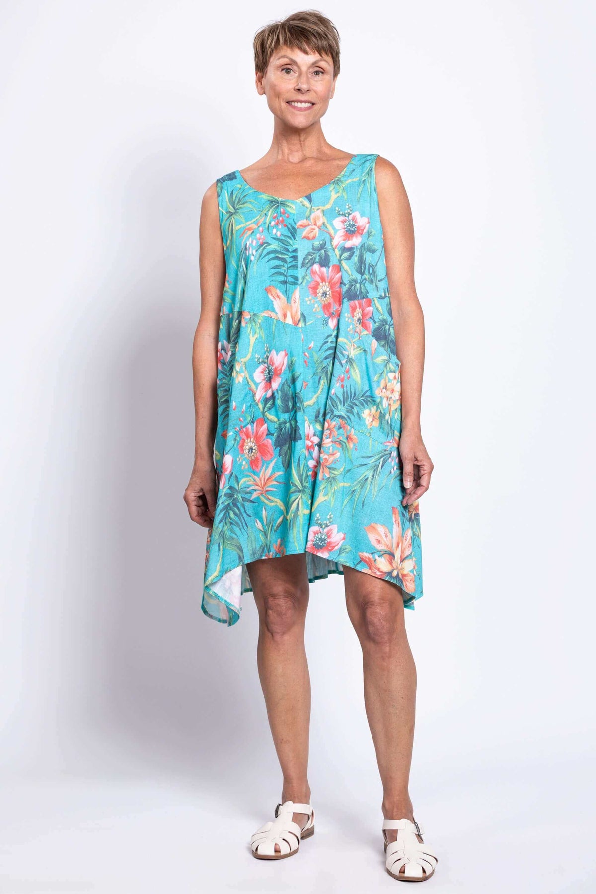 Front view of a woman in a turquoise tropical print sleeveless dress with uneven hem