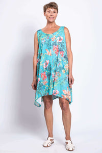 Front view of a woman in a turquoise tropical print sleeveless dress with uneven hem