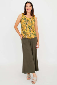 Woman smiling in yellow tropical sleeveless tank and olive wide-leg pants, hand in pocket, front angle