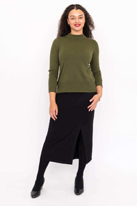 Front angle of a woman wearing an olive green sweater and black skirt