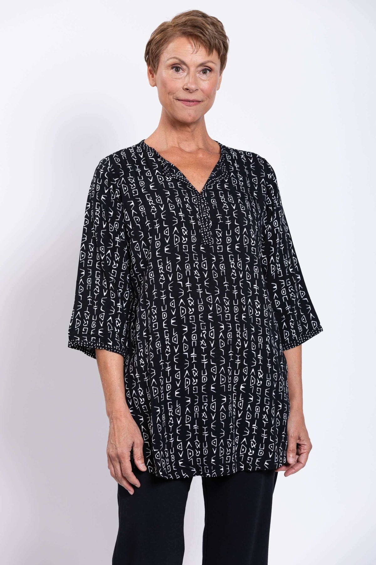 Front closeup view of a woman wearing a black tunic with white abstract print