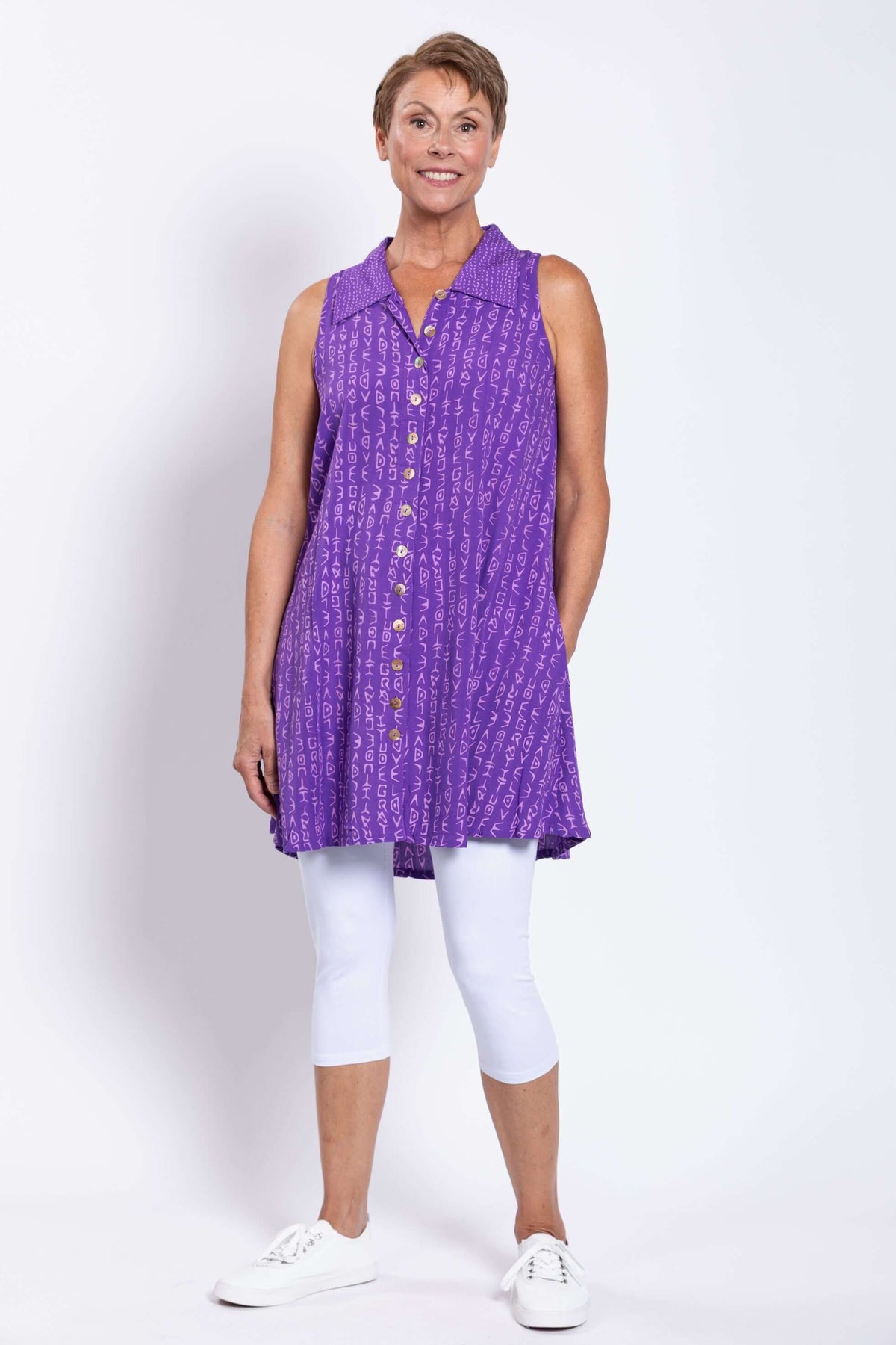 Full front view of woman smiling and modeling a violet sleeveless shirt tunic with white shoes