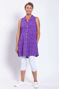 Full front view of woman smiling and modeling a violet sleeveless shirt tunic with white shoes
