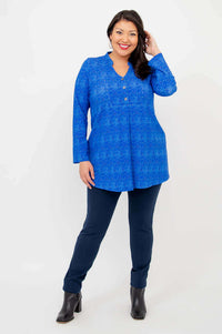 Model posing in a blue tunic top and navy pants, with hand near hair, front view