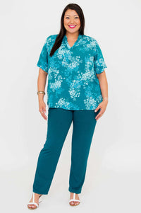 Front view of a woman wearing teal floral Reni Top and teal pants, standing confidently