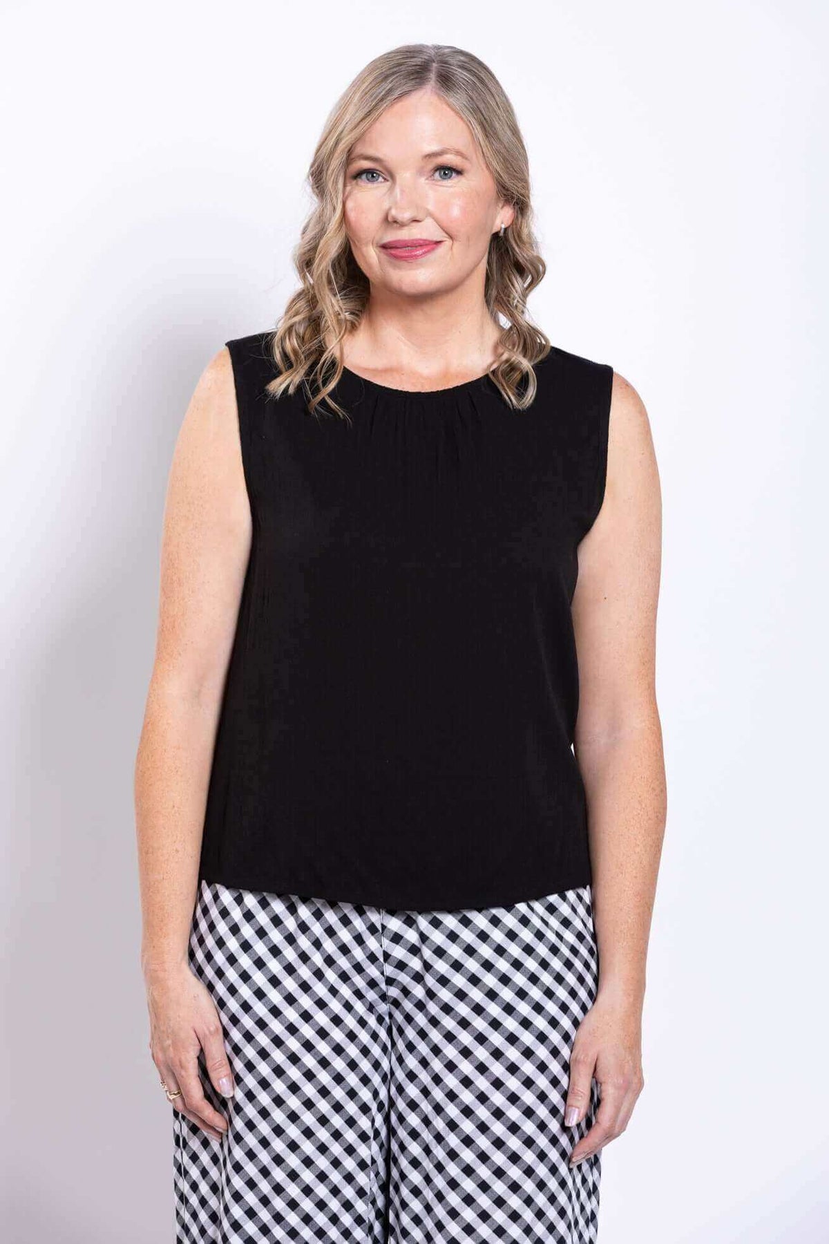 Front view of woman modeling sleeveless black top and gingham pants
