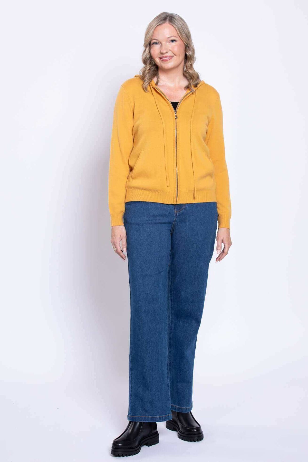 Front relaxed pose of a woman in blue straight leg jeans and a yellow hoodie.