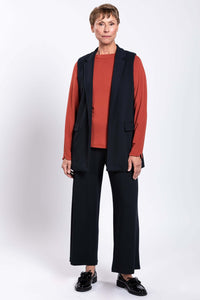 Front view of model in black open front vest, matching pants, and rust long sleeve top