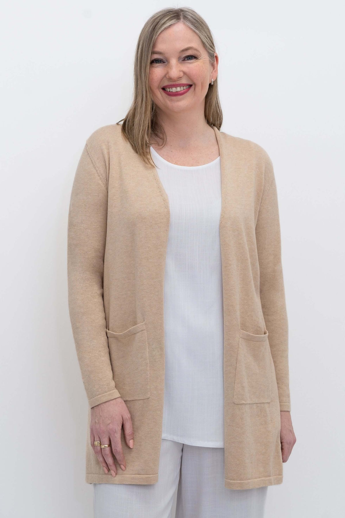 Front view of woman wearing a beige open cardigan sweater with patch pockets