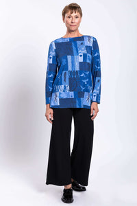 Front view of woman standing in blue patchwork top with black wide-leg pants