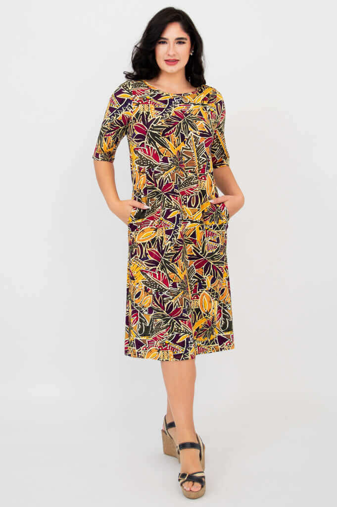 Front view of woman wearing Olivia dress in colorful Tropikal print with hands in pockets