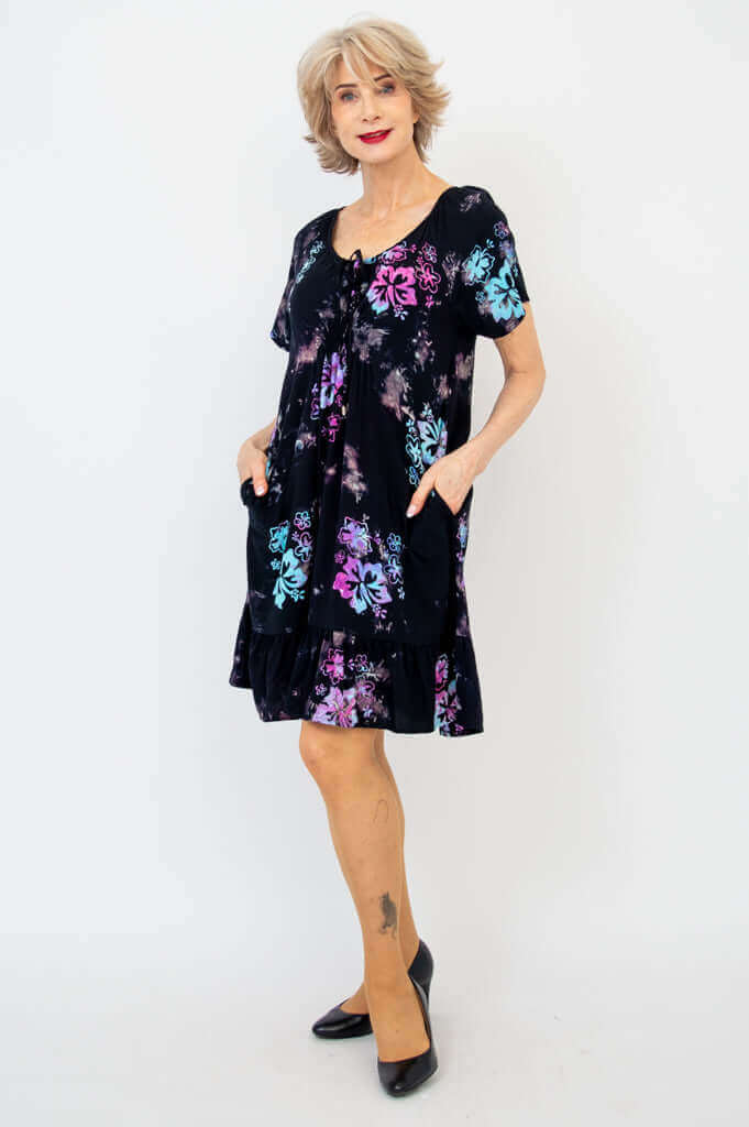 Front view of woman wearing black dress with colorful floral pattern and pockets
