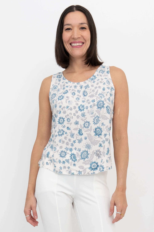Front view of woman wearing a blue floral scoop neck tank top and white pants