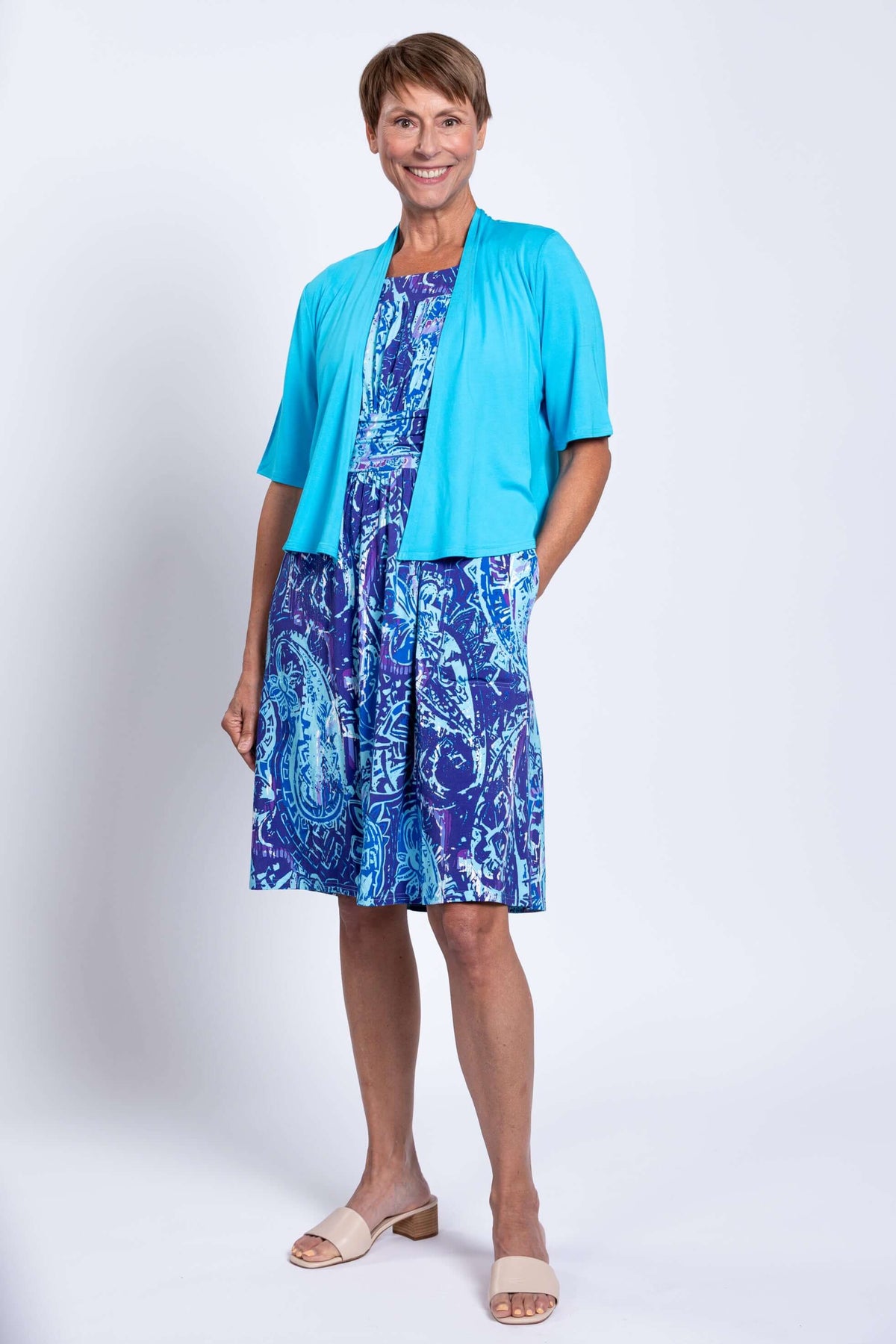 Front view of a woman in a blue paisley dress paired with a turquoise shrug