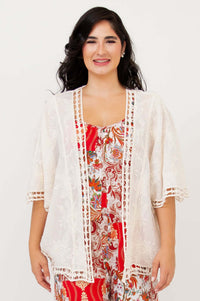 Front view of a woman wearing a lace boho kimono cardigan over a red floral dress