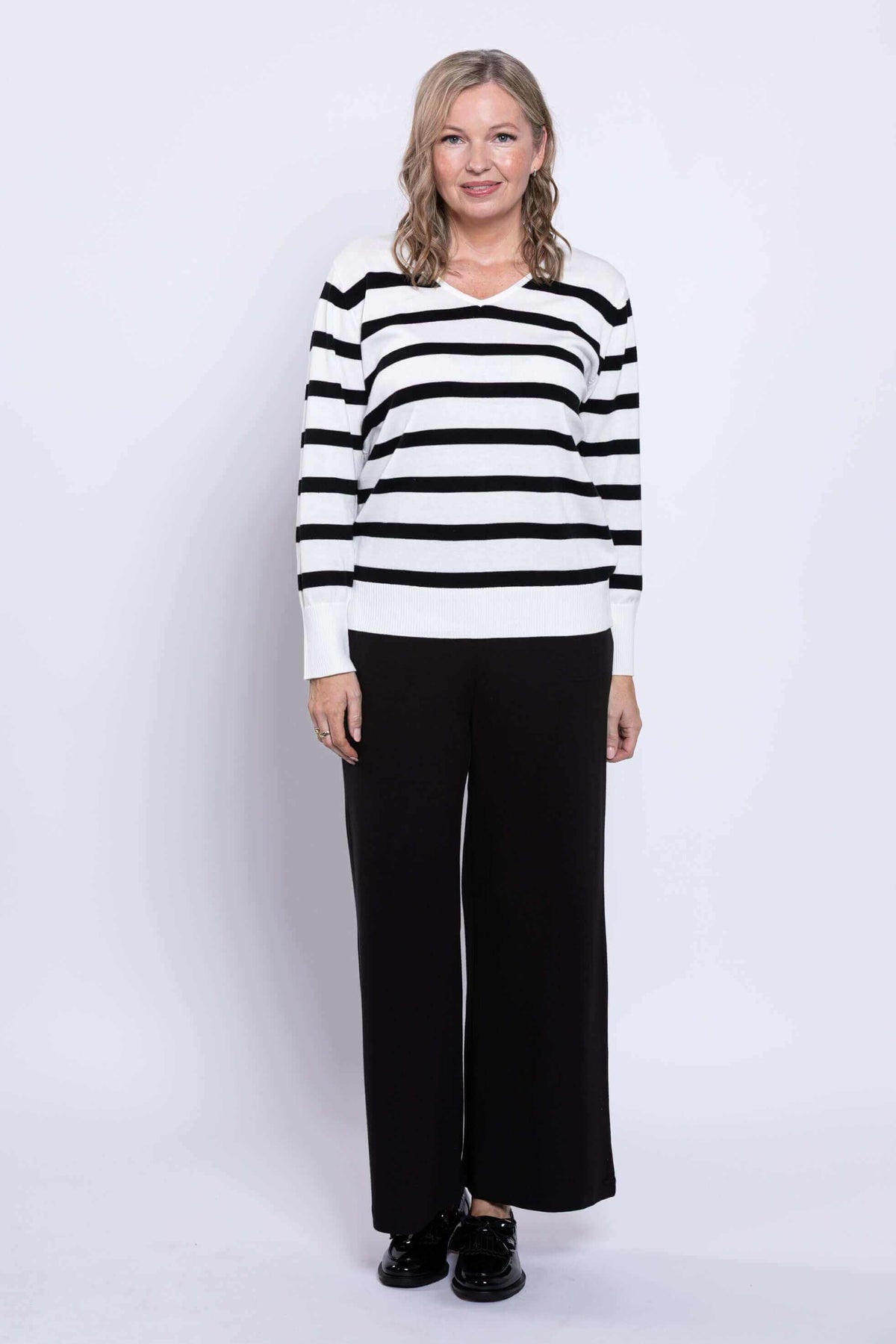 Woman wearing a black and tan Breton stripe V-neck sweater and black pants, front view