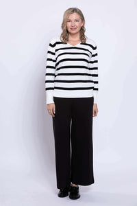Woman wearing a black and tan Breton stripe V-neck sweater and black pants, front view