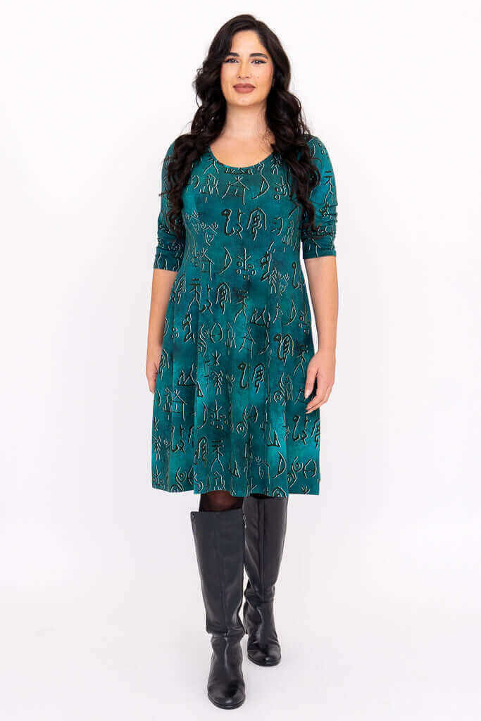 Front view of woman wearing a teal dress with petroglyph pattern and black knee-high boots