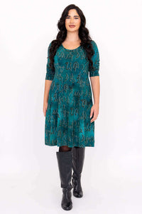 Front view of woman wearing a teal dress with petroglyph pattern and black knee-high boots