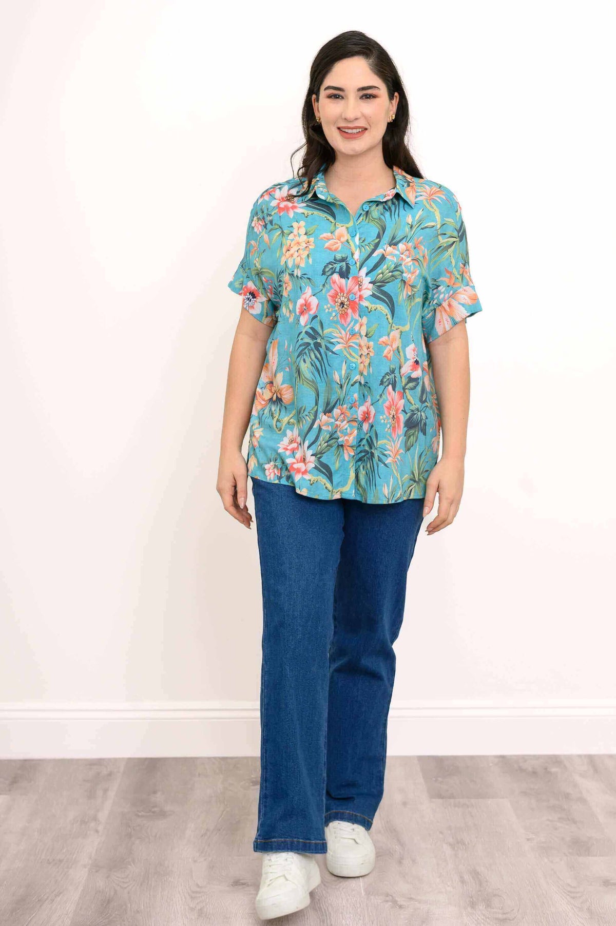 Front view of woman modeling a teal floral blouse paired with jeans and white sneakers